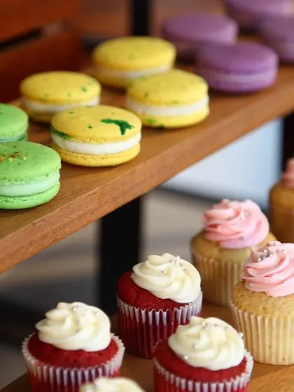 A vibrant display of macarons and cupcakes on a wooden stand. This image captures the colour and variety of our small dessert offerings, perfect for any celebration.