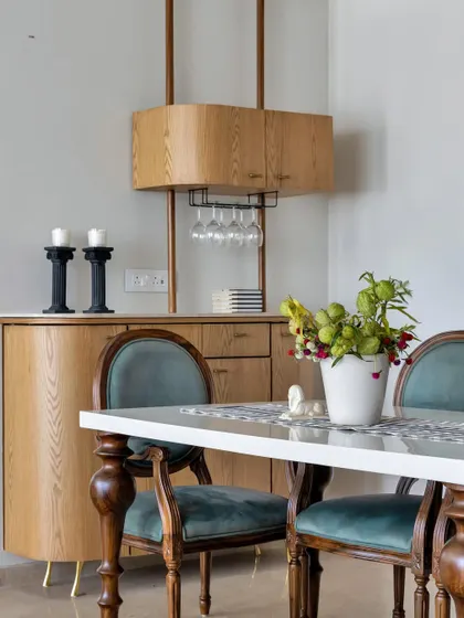 This dining area features a sophisticated bar cabinet, perfect for entertaining. The classic wooden chairs with teal velvet upholstery add a touch of vintage glamour, while the modern bar unit provides practical storage.