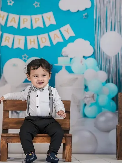 A smiling little boy enjoying his first birthday photoshoot. The blue and silver decorations create a classic and festive look.
