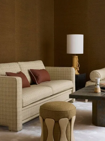 A serene living room where our Nobilis fabrics create a grounded, elegant atmosphere. The sofa and ottoman are upholstered in tactile, earthy-toned textiles that coordinate beautifully with the textured brown wallcovering.