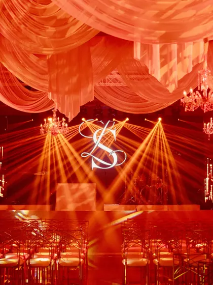 The stage is set with the couple's custom 'SL' monogram, illuminated by spotlights, creating a focal point for the Sangeet night.