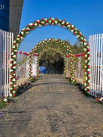 A series of classic floral arches made with red and white roses, creating an elegant and timeless pathway for a wedding entrance.