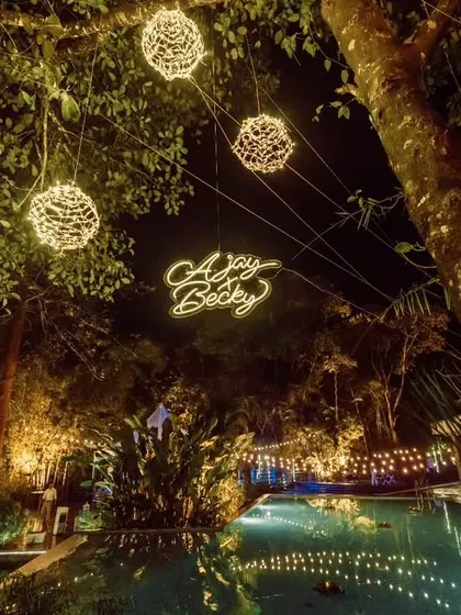 A romantic poolside reception setting at The Ibnii, Coorg, with the couple's names in a custom neon sign, surrounded by magical string lights.