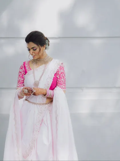 A simple and elegant portrait of a bride in a white and pink sari, looking down with a gentle smile.