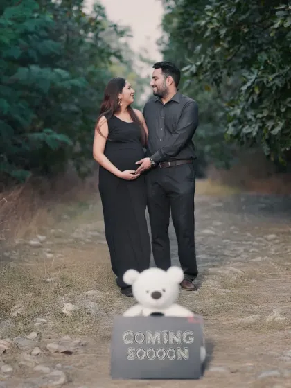 A creative announcement shot with a teddy bear and a "Coming Soon" sign in the foreground. The couple stands lovingly in the background, creating a photo with a beautiful sense of depth and story.