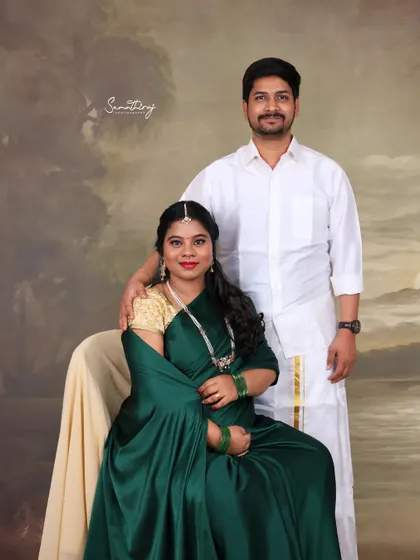 A classic studio portrait of a couple in traditional South Indian attire. Their formal pose and the painterly backdrop give the image a timeless and elegant quality.