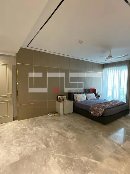 A spacious master bedroom with a minimalist aesthetic, featuring a grey marble floor, a large upholstered headboard, and a sleek, integrated ceiling light design.