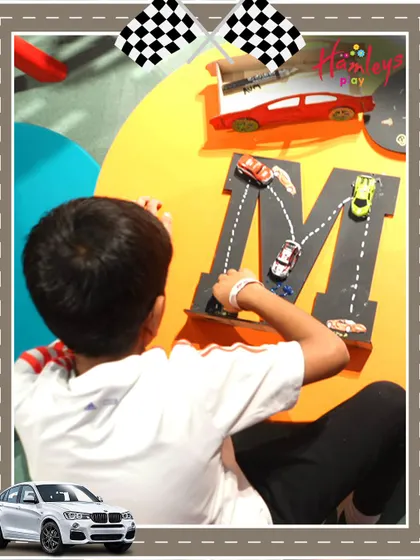 Another creative station at our Mini Racers event, where a child uses toy cars to trace the letter 'M'. I love incorporating educational elements into our play activities.