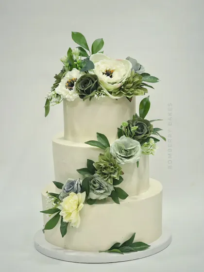 A simple yet stunning three-tier buttercream cake with a cascade of green and white sugar flowers.