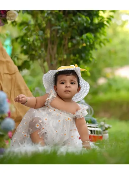 A little sunshine in the garden. This sweet outdoor portrait captures a baby girl in a daisy dress, enjoying a beautiful day.
