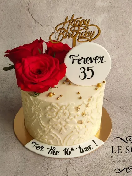A fun and stylish cake to celebrate a milestone birthday. This half-kg Cashew Butterscotch Crunch cake has a beautiful white lace stencil design, topped with fresh red roses and a cheeky "Forever 35" message.