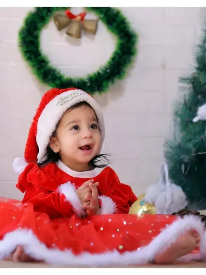A happy baby girl in her Santa dress, surrounded by festive decorations during our special Christmas mini-sessions.