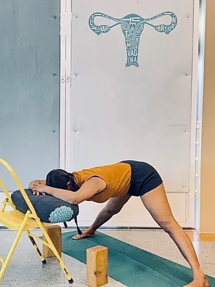 This supported forward bend over a chair in Prasarita Padottanasana (Wide-Legged Forward Bend) is deeply restorative. It calms the nervous system, releases the lower back, and gently stretches the hamstrings, making it an accessible pose for many.