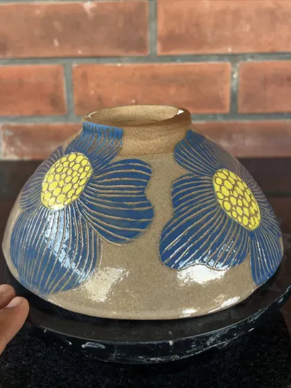 A student's wheel-thrown bowl decorated with large, stylized flowers using the sgraffito carving technique.