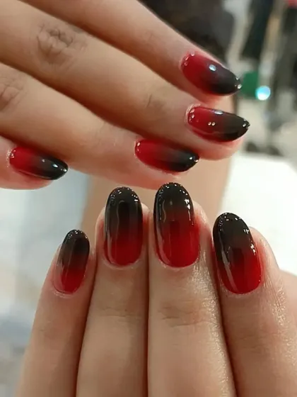 A dramatic red and black ombre on almond-shaped nails, blending from a bright red base to a deep black tip.
