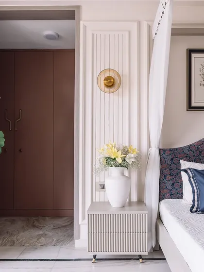 A detail shot showing the custom bedside table with a fluted front and a statement wall sconce. The rich brown wardrobe in the background provides a beautiful contrast.