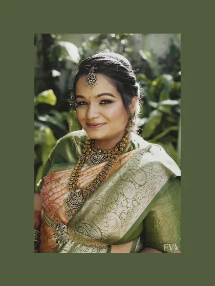 A classic portrait of a woman in a beautiful green and pink silk saree, adorned with heavy antique silver jewellery. The natural, leafy background complements the traditional attire, making it ideal for a maternity or family photoshoot.