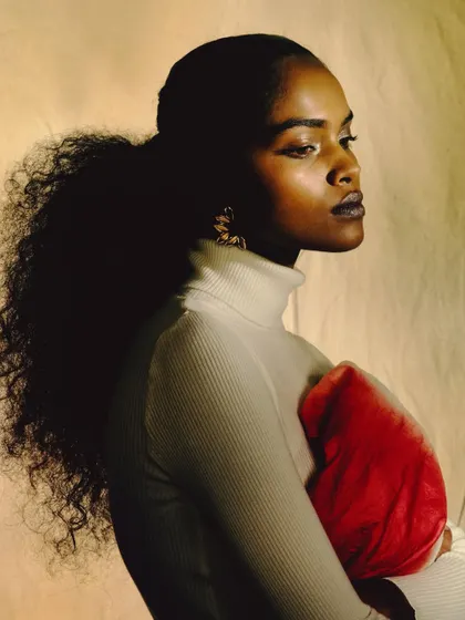 A three-quarter portrait where the model holds a piece of red fabric. The warm, painterly light and thoughtful expression create a soft and intimate moment.