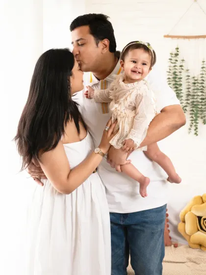 A tender family moment, with dad kissing mom's forehead while holding their happy baby.