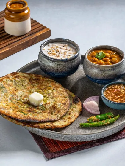 A breakfast platter of Amritsari Chole with Aloo Paratha, served with raita and pickle for an authentic Punjabi meal.