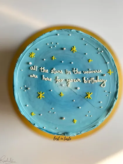 A dreamy birthday cake with a blue ombre buttercream base, decorated to look like a starry night sky with a hand-piped message.