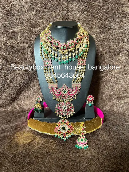 A stunning Jadau-style bridal set with red and green stones and green bead drops. This rental includes multiple necklaces, earrings, maang tikka, and a vaddanam.