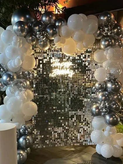 A glamorous silver and white balloon arch against a sparkling sequin backdrop. This setup is perfect for an elegant evening celebration, creating a festive and glittering atmosphere.
