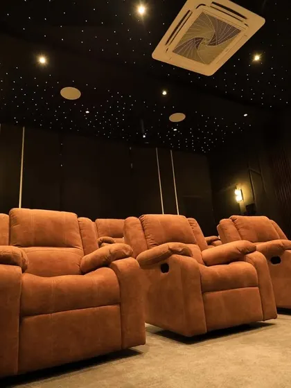This luxury home cinema in Pudukottai features warm, earthy tones with its brown recliners and dark, wood-paneled walls. The starlit ceiling and wall sconces add a touch of magic.