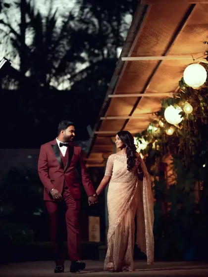 A stylish couple walks hand-in-hand at their evening reception, captured in a candid, cinematic style.