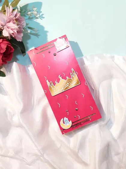 A vibrant pink Eidi envelope with a golden mosque cutout.