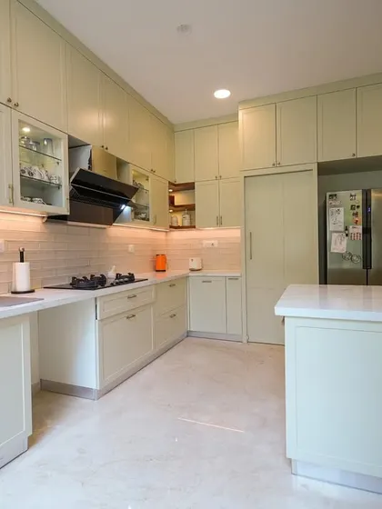 The soft sage green cabinetry in this kitchen adds a refreshing, earthy warmth, while the white marble countertops and island enhance the sense of brightness and openness.