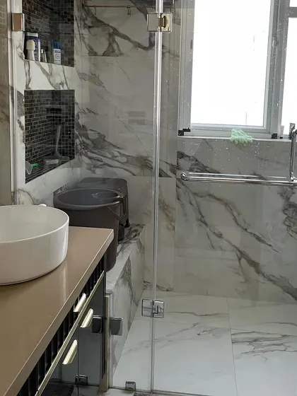 This view shows the layout of the marble-themed bathroom, including the spacious glass-enclosed shower area. The large window allows for plenty of natural light.