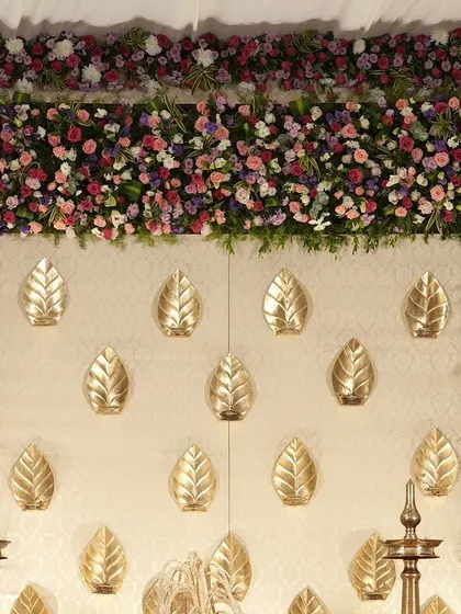 A close-up of the cream and gold backdrop, where golden leaves are mounted on the wall and framed by a dense border of colorful flowers.