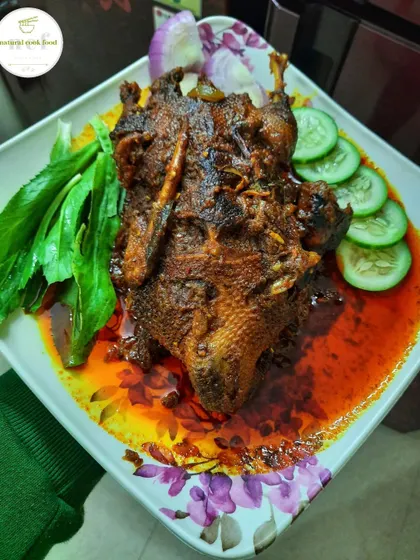 A plated 'Nganu mapum' or whole duck curry, garnished with fresh herbs and cucumber.