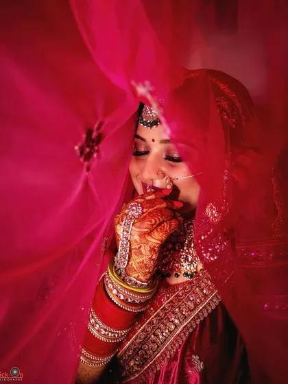 A candid, shy smile captured through the bride's red veil, an intimate and beautiful moment.