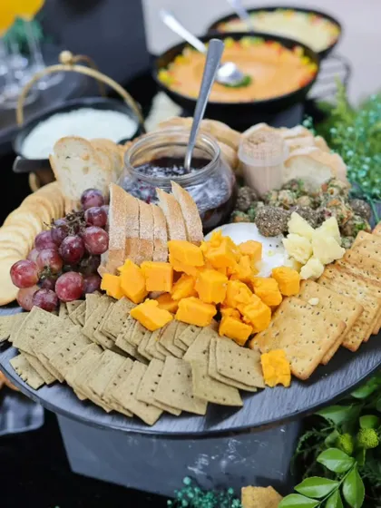 A beautiful charcuterie board featuring a variety of cheeses, crackers, and dips, surrounded by lush greenery. This showcases our skill in creating visually stunning food displays.
