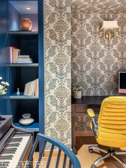The music room at Sunlit Serenity is separated from the dining area by an elegant glass partition. The room itself has a moody, dark aesthetic with deep navy walls and patterned wallpaper.