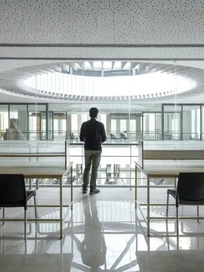 A solitary figure in the Sona Library, a project celebrated for its thoughtful interiors. The design uses natural light from a central oculus and clean lines to create a tranquil space for reflection and study.