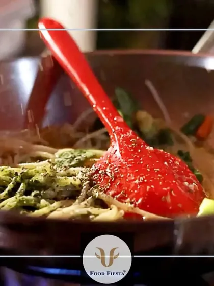 A close-up of spaghetti being tossed in a pan with a vibrant pesto sauce and fresh vegetables. This is comfort food elevated to a gourmet experience.