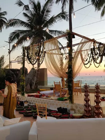 A wider view of the rustic beach wedding, showing the mandap and guest seating. The combination of natural textures, warm lighting, and the sunset creates a truly magical and inviting atmosphere.