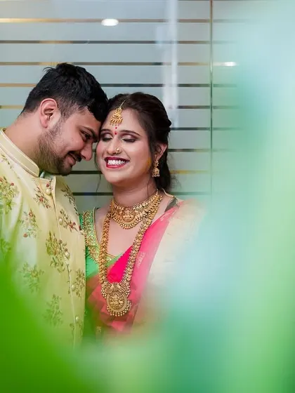 A tender moment between a couple, their foreheads touching, framed by soft green foliage.