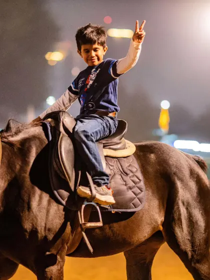 A young boy flashes a victory sign, thrilled with his night-time riding adventure. Our evening sessions are fun for the whole family.
