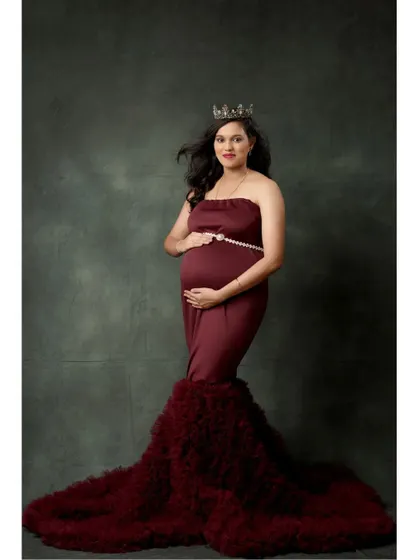 A full-length view of the wine-red maternity gown, showcasing the long, ruffled trail and the simple pearl belt accessory.