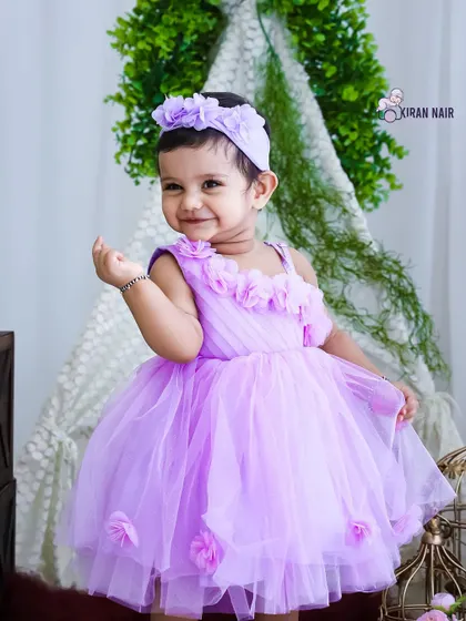 A smiling toddler girl dressed in a lovely lavender party dress. This studio portrait, set against a teepee backdrop, is perfect for a pre-birthday or milestone photoshoot.
