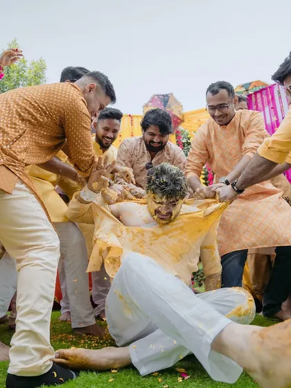 The groom's friends enthusiastically pulling at his kurta during the haldi ceremony. This photo is a testament to the fun and wild traditions among friends.