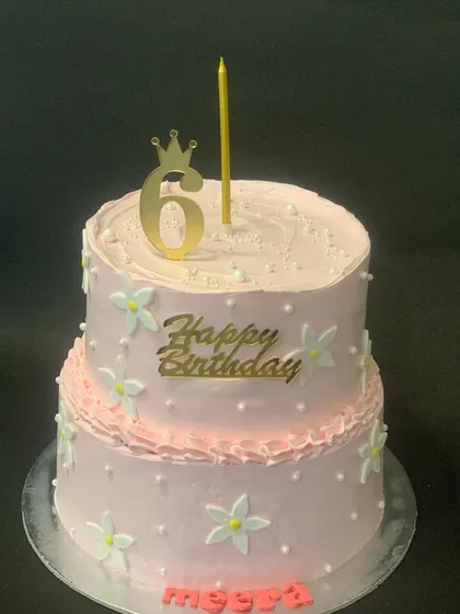 A pretty and elegant two-tier pink birthday cake. The simple design is decorated with small white flowers and pearls, perfect for a sweet 6th birthday.
