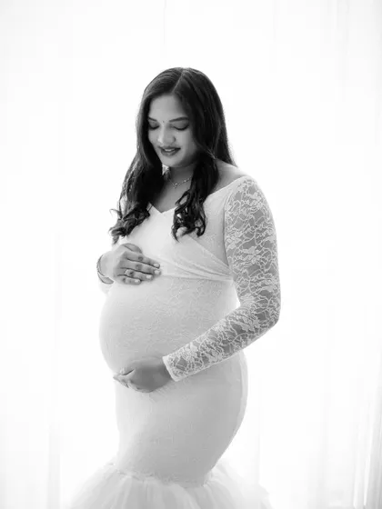 A high-key black and white portrait of a mom-to-be in a beautiful lace gown. The soft lighting creates a gentle and serene mood.