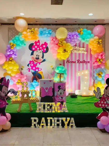 A colorful and fun Minnie Mouse theme for a first birthday party, featuring plenty of pink, character cutouts, and a playful, grassy stage setup.