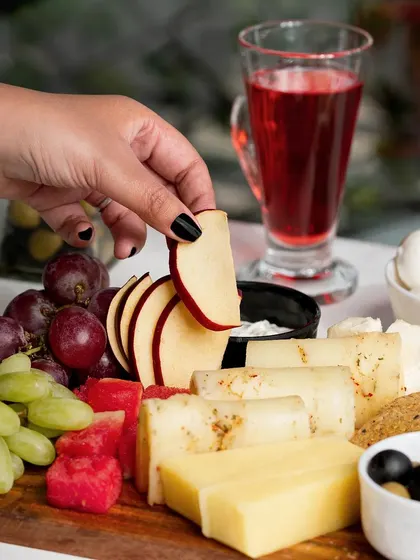 A lifestyle shot of a hand picking an apple slice from a cheese board. Including a human element makes the scene more engaging and relatable.