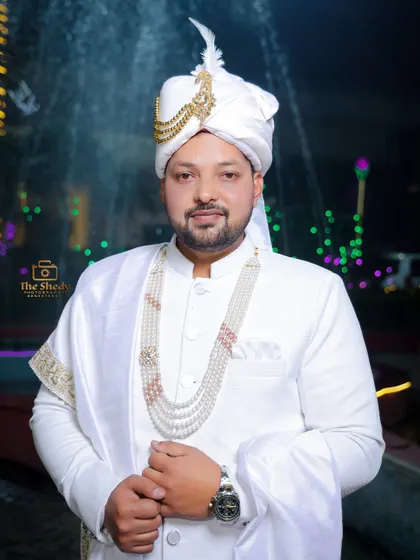 A classic portrait of a groom in a white sherwani, posing in front of a fountain at night. A simple, elegant, and timeless shot.